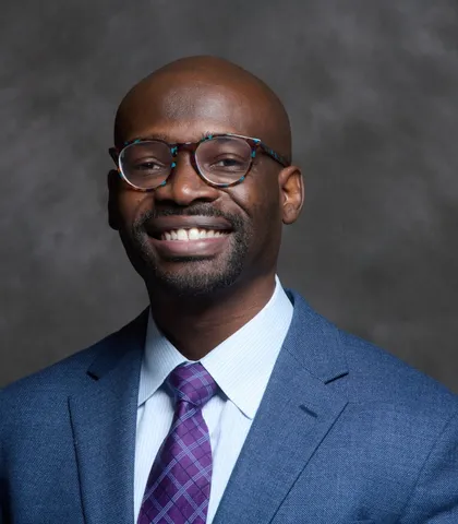 Dr. Jeff Bullock smiling, wearing glasses, a blue suit and a purple tie
